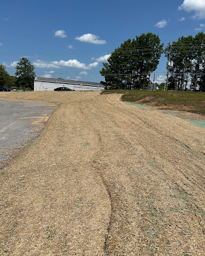 Erosion control blanket rolled over a freshly seeded slope beside a commercial building